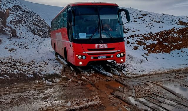 Bus rojo de Atacama avanzando por un camino con nieve